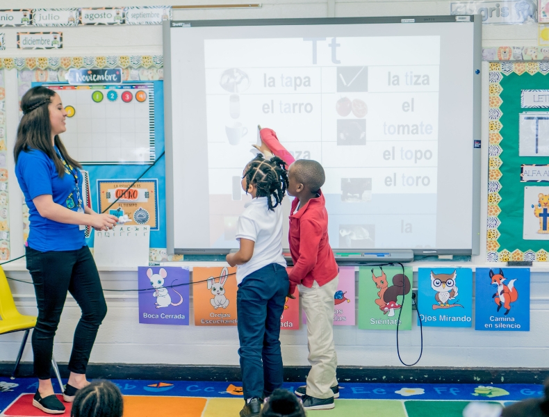 A Spanish dual language program classroom with a teacher and two students at a Smart Board