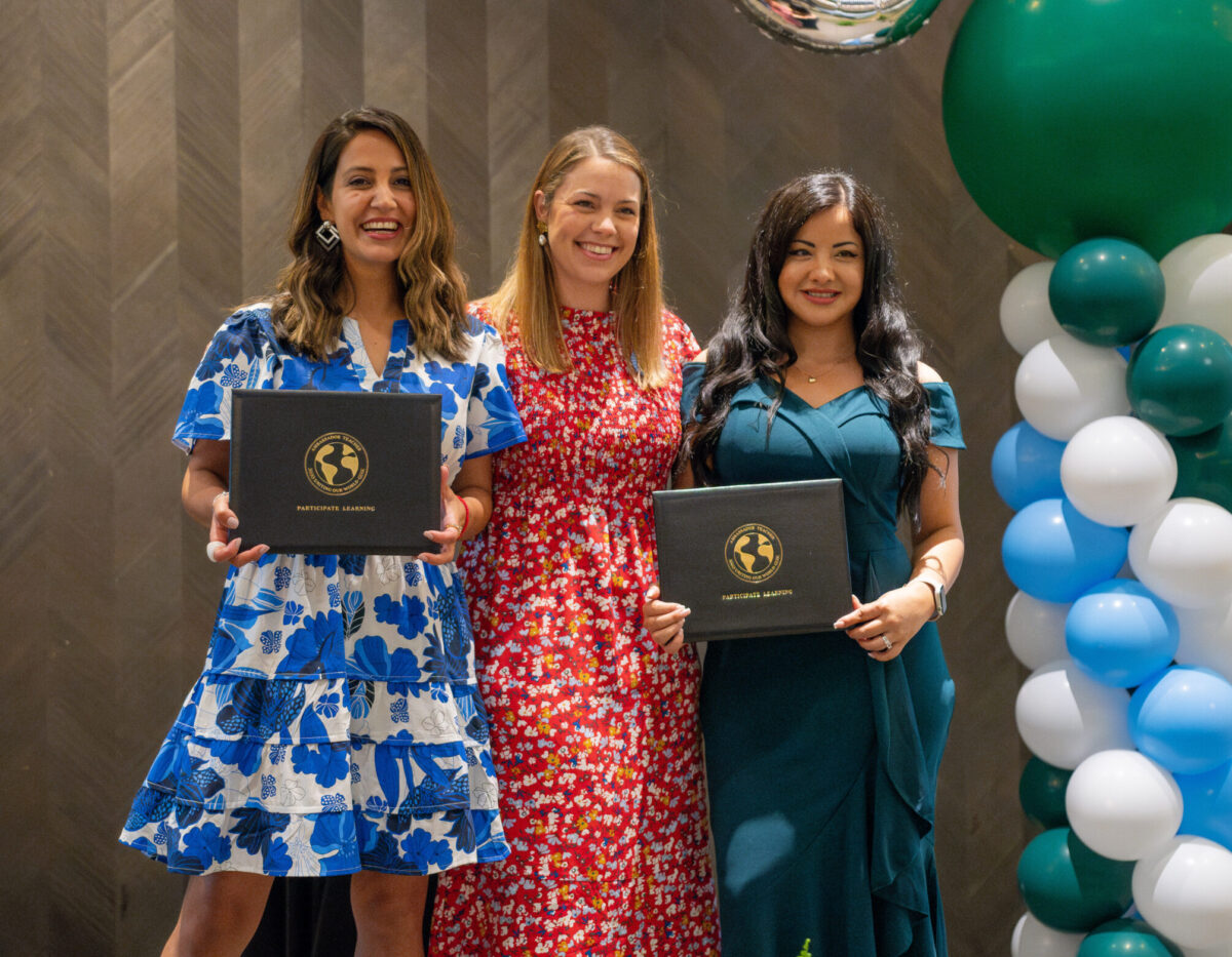 Two Ambassador Teachers pose for a picture with their program manager while holding their diplomas
