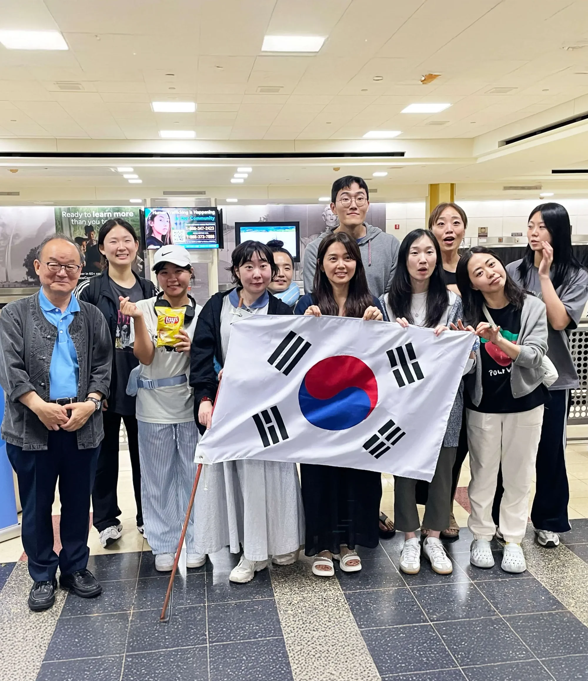 Group of South Korean teachers arriving in the United States at an airport terminal, proudly holding the South Korean flag as they begin their journey to teach in the USA through the J-1 visa cultural exchange program, supported by Participate Learning, an official visa sponsor for international educators.