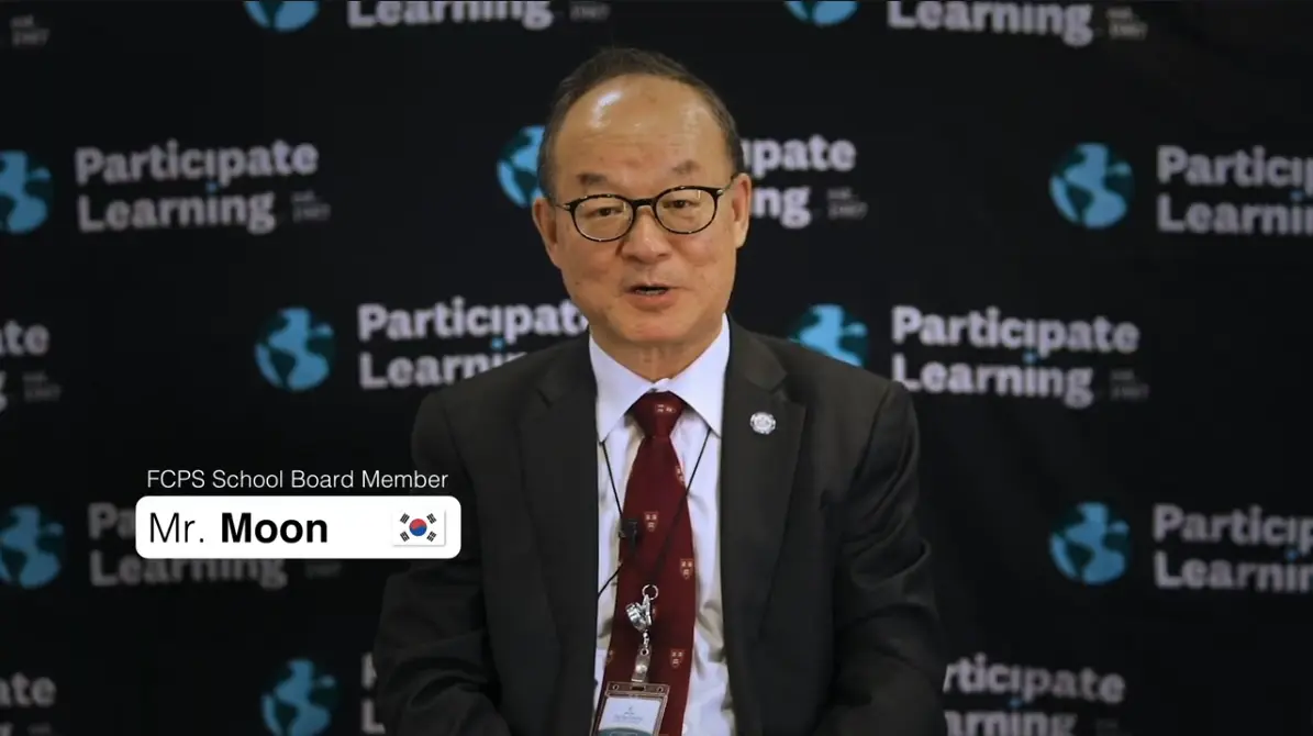 Mr. Moon, a South Korean FCPS School Board Member, speaking in front of a Participate Learning backdrop during a formal event, highlighting his support for the J-1 visa cultural exchange program and international teachers arriving to teach in the USA through Participate Learning.