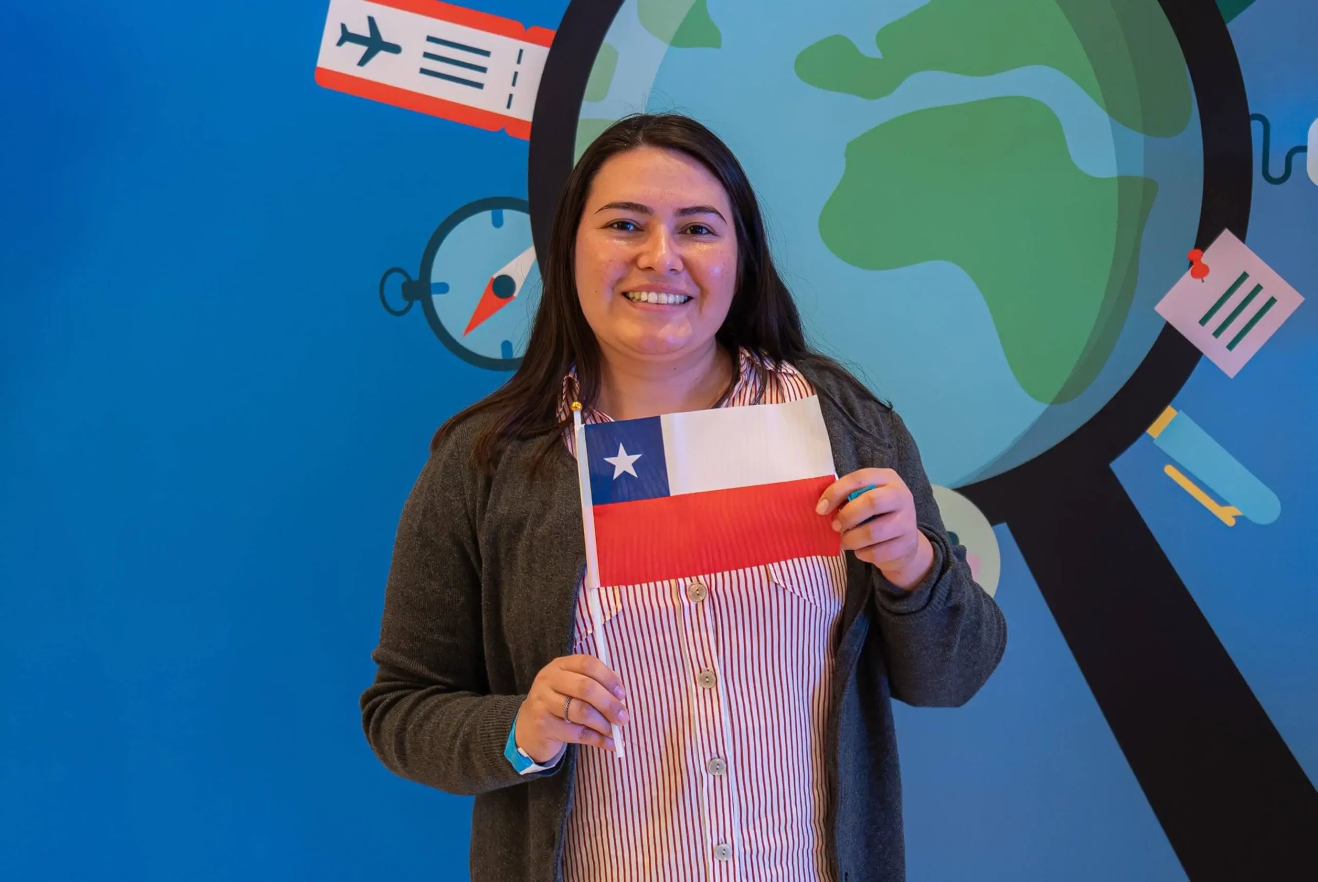 Female teacher from Chile holding the Chilean flag in front of a globe-themed background at Participate Learning orientation, part of the teach in the USA initiative for educators from Chile.