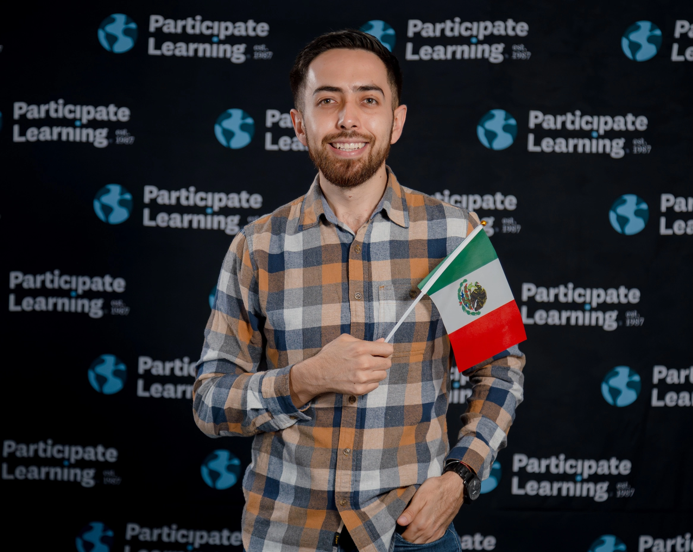 Teacher from Mexico poses with the Mexican flag in front of the Participate Learning backdrop during orientation, representing his country as part of the exchange program.