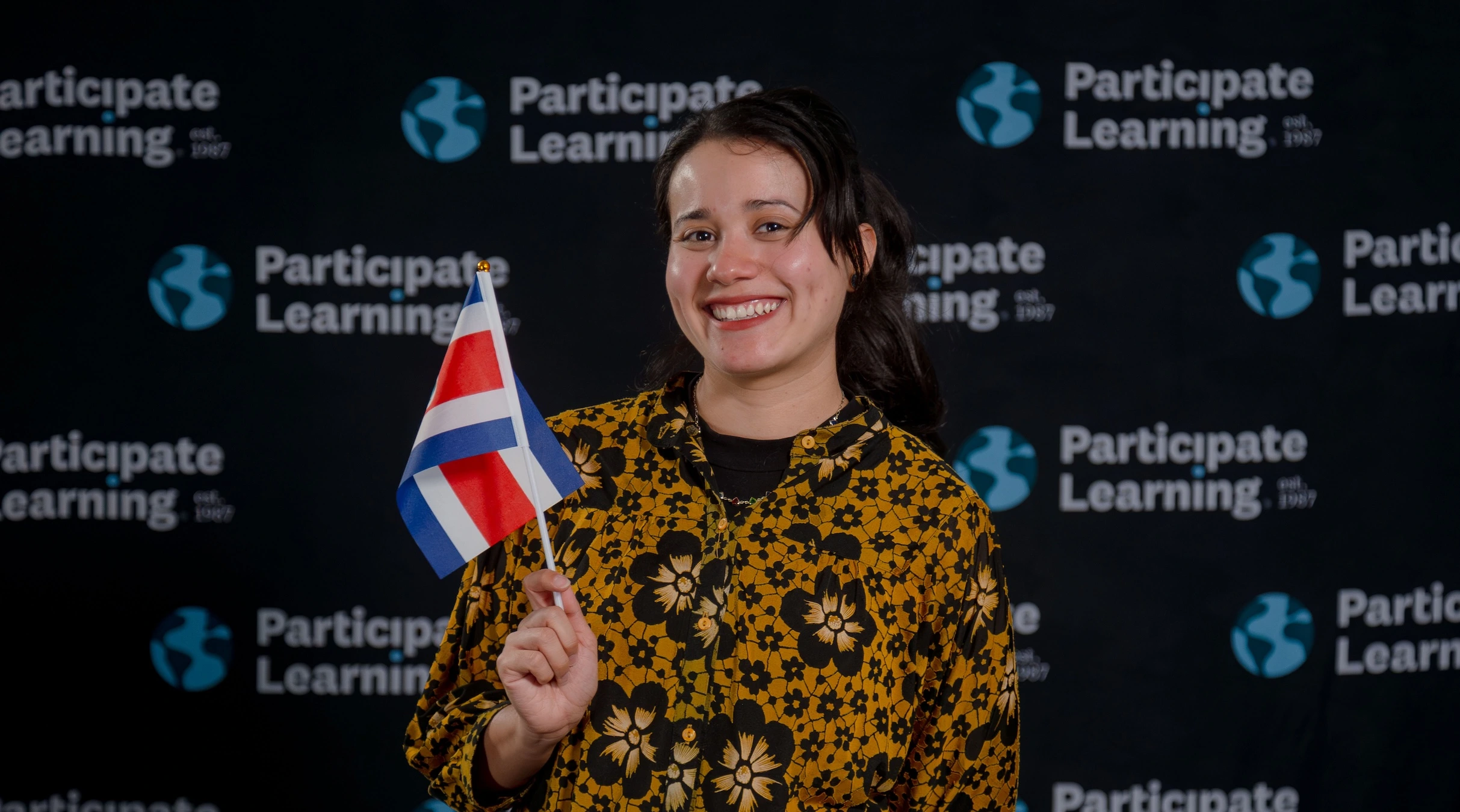 Teacher from Costa Rica poses with her country’s flag in front of the Participate Learning backdrop, celebrating the start of her teaching journey in the United States.