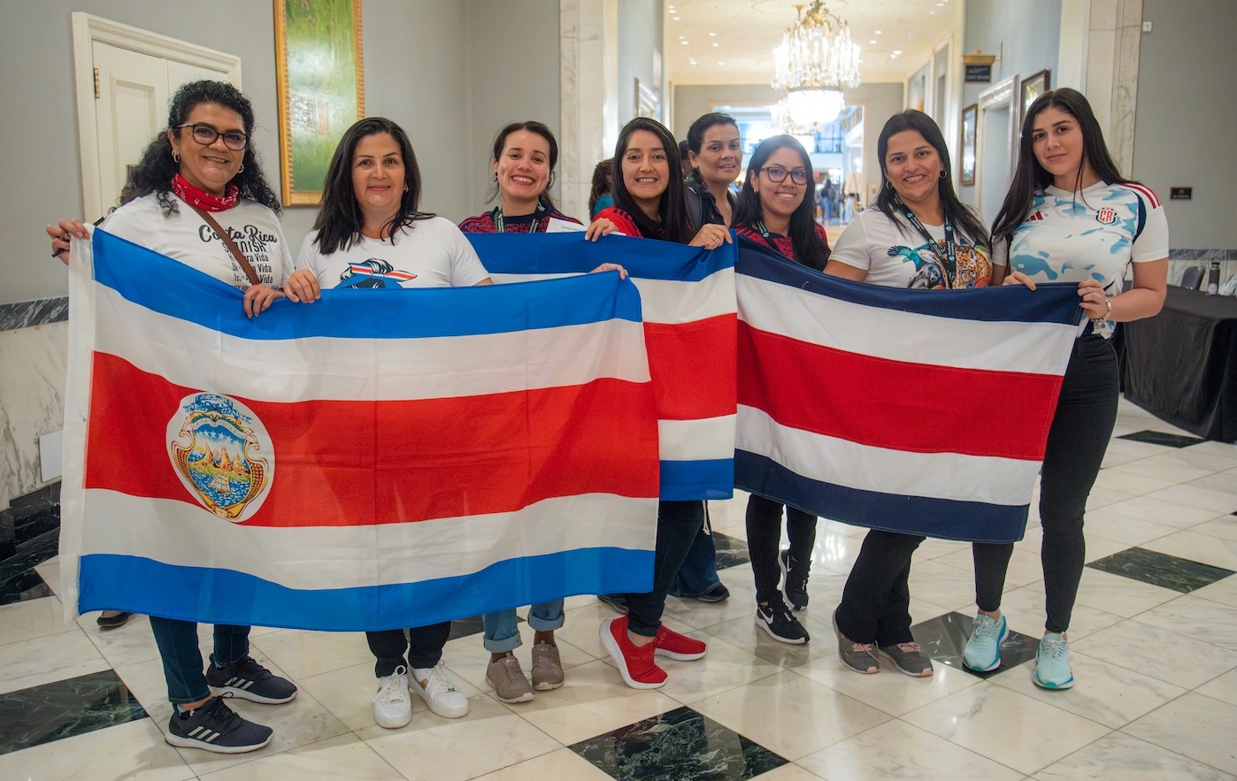 Group of 8 teachers from Costa Rica hold their national flag together at Participate Learning orientation, marking the start of their cultural exchange teaching experience in the United States.