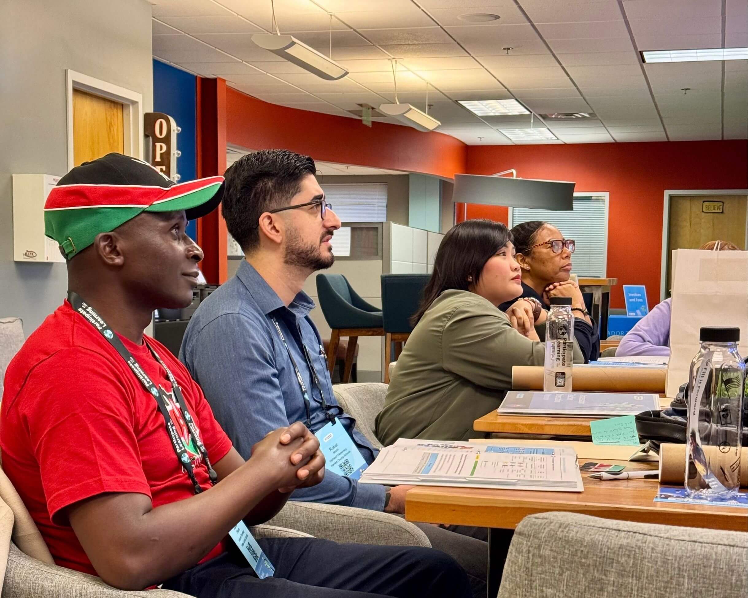 Four teachers seated at tables, listening attentively to a presentation during their arrival orientaiton.