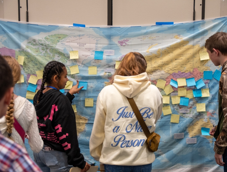 Students in front of a world map at the Conexiones para la Acción Diplomática event at UNC Greensboro