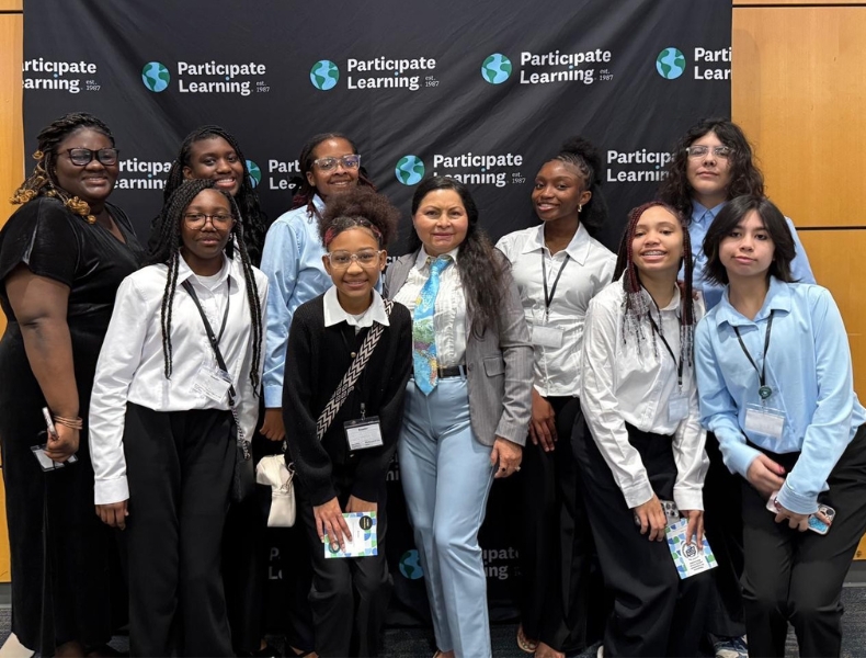 Group of middle school students pose for a photo with their teacher in front of a Participate Learning backdrop at the Conexiones para la Acción Diplomática event.