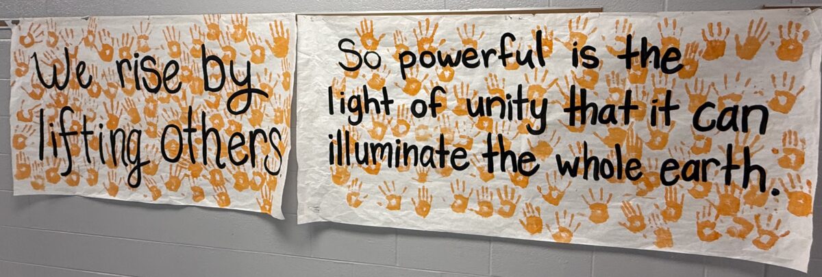 Student-created banners with painted handprints and the messages "We rise by lifting others up" and "So powerful is the light of unity that it can illuminate the whole earth."