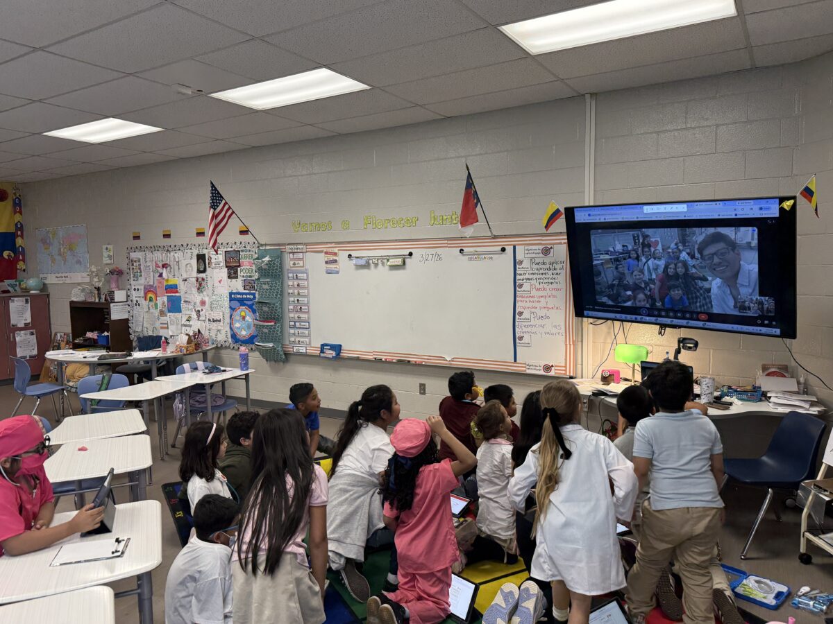 Students participating in a virtual classroom exchange during a Spanish dual language lesson, practicing authentic language use and global learning by connecting with peers on a video call.