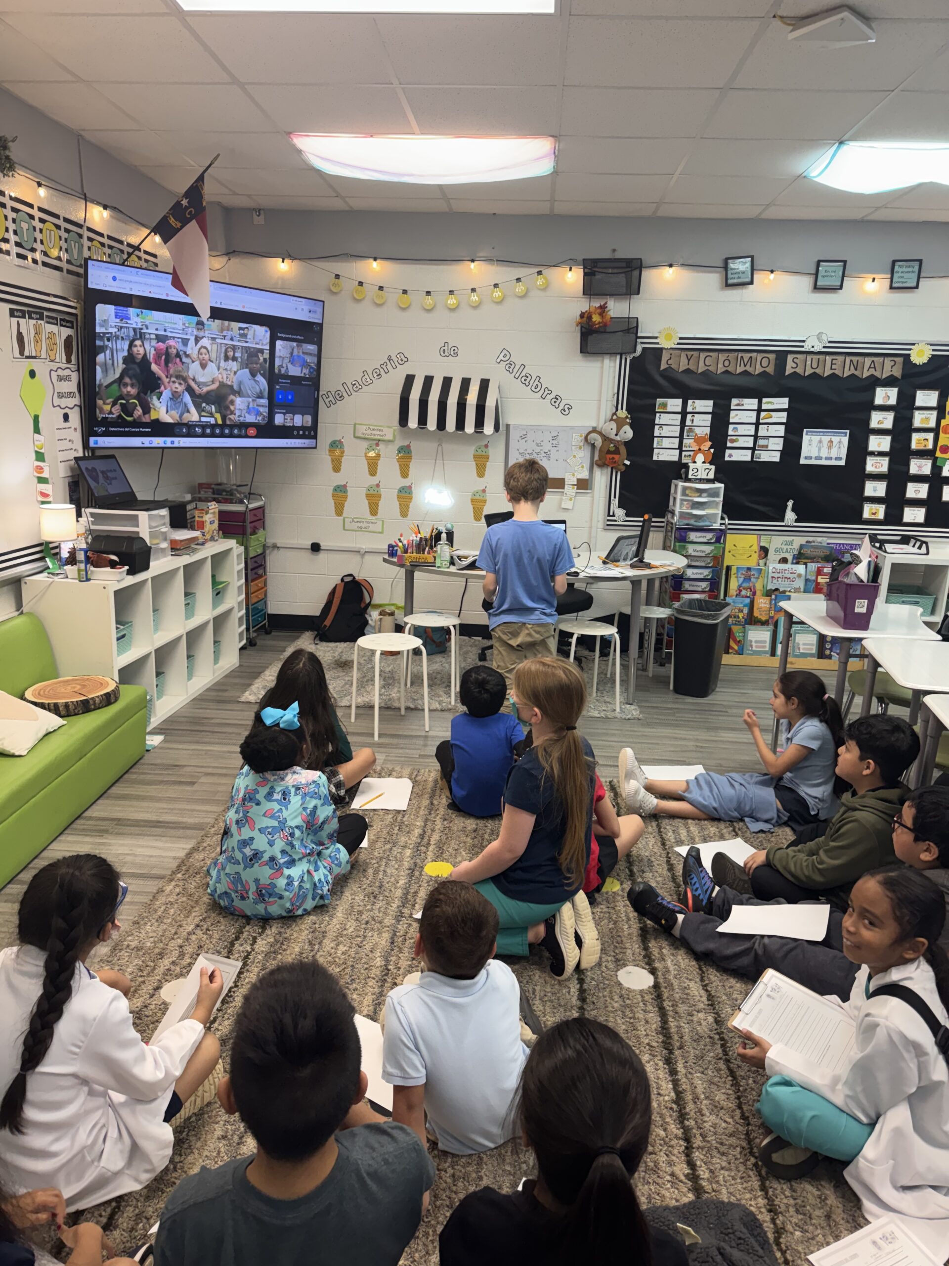 Students participating in a virtual classroom exchange during a Spanish dual language lesson, practicing authentic language use and global learning by connecting with peers on a video call.