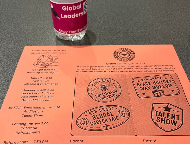 A coral-colored event program for Grandview Middle School's Global Leaders Showcase, displayed on a table next to a branded water bottle.