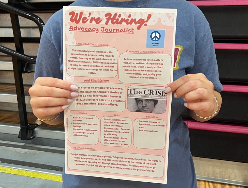 A student holds up a "We're Hiring! Advocacy Journalist" flyer styled as a job posting, connecting the role to the global challenge of promoting peace. Sections include job description, duties, skills, and education.