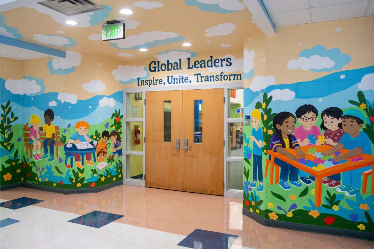 School hallway mural showing children reading, exploring nature, and solving a puzzle beneath the words “Global Leaders: Inspire, Unite, Transform.”